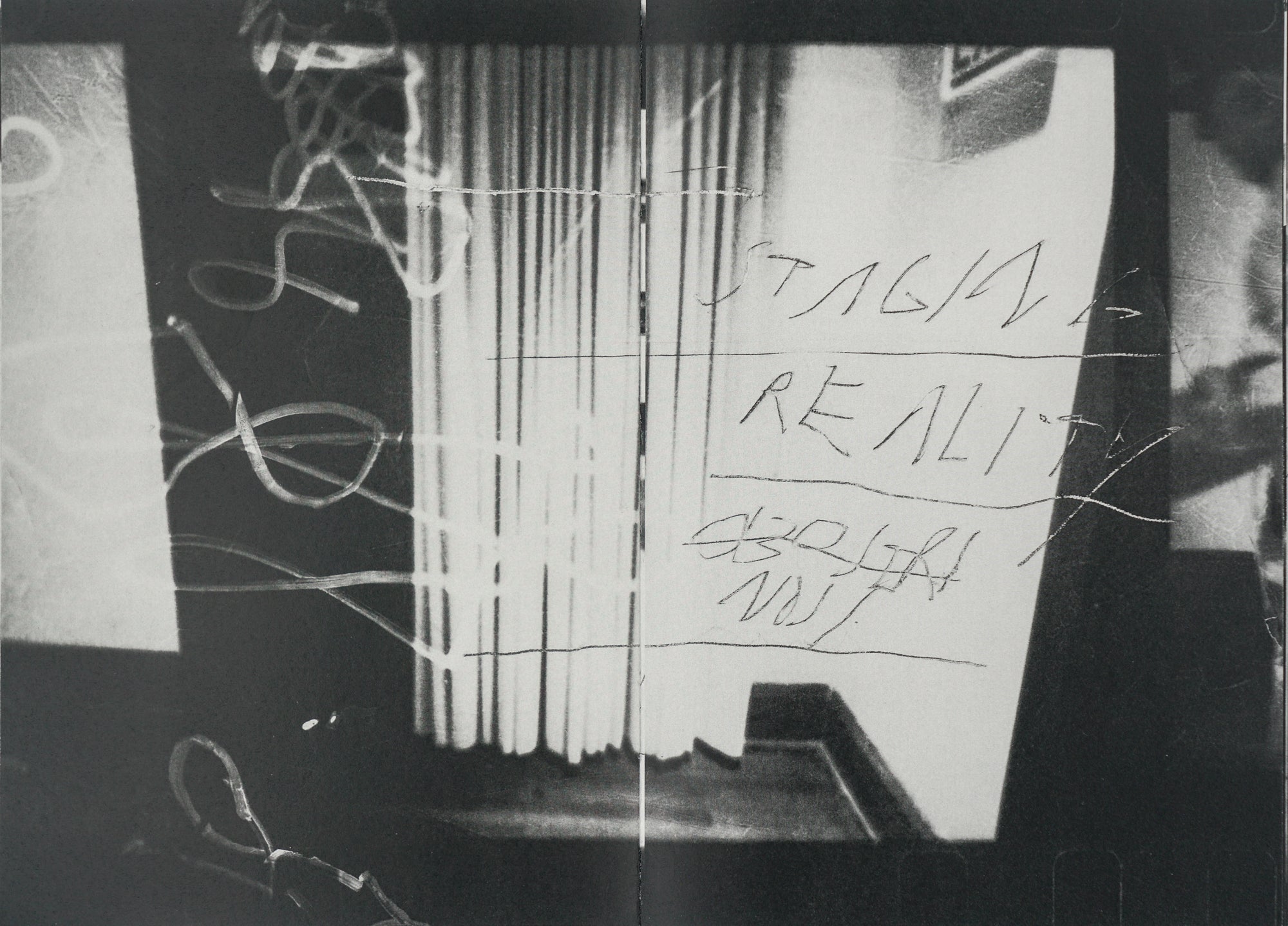 Spread from the book—a grainy black-and-white photograph of the corner of a room with curtains. STAGING REALITY and other illegible writings are scrawled on the image.