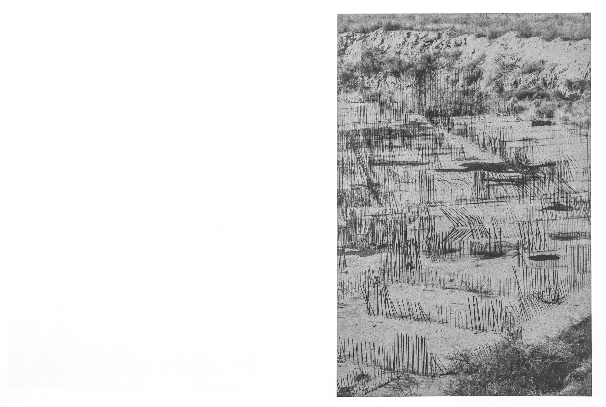 A spread depicting a low contrast black and white photograph of a metal wires sticking out upwards from the ground in a sandy landscape.