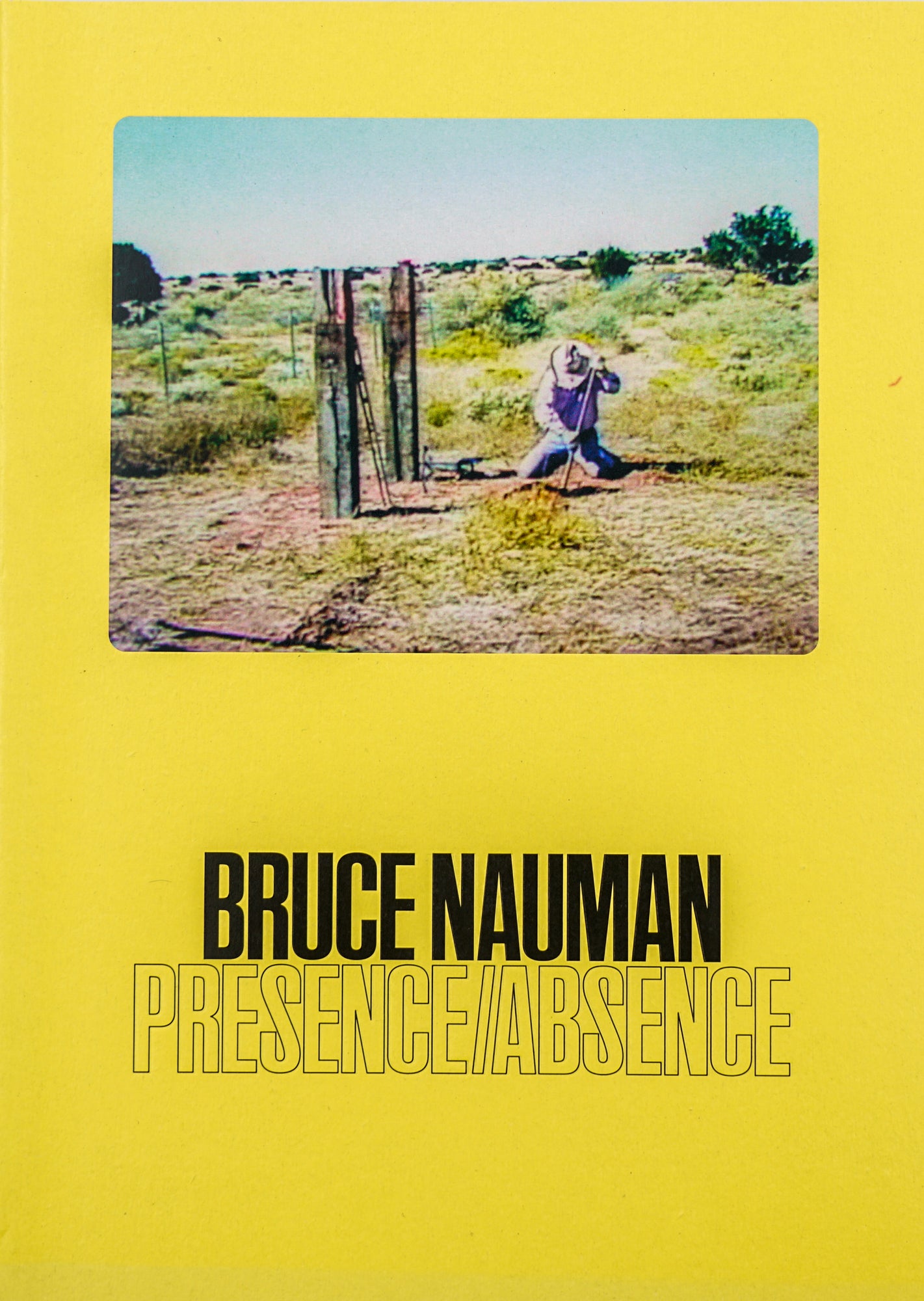 Book cover in monochrome yellow with the title and artist BRUCE NAUMAN PRESENCE/ABSENCE written in sans serif black on the lower half of the page. On the upper half of the picture is a color image of a man kneeling in a field with hills and bushes in the background.
