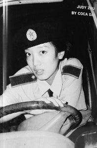 Black and white close-up photograph of woman in uniform leaning on a motor vehicle wheel.