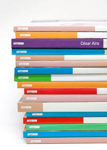 Book cover with a stack of Artforum magazine, each in a different vibrant color. One of the spines of the stack of books has the author's name, César Aira.
